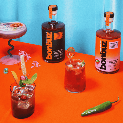 Two bottles of Bonbuz non-alcoholic functional spirit on an orange table with cocktails