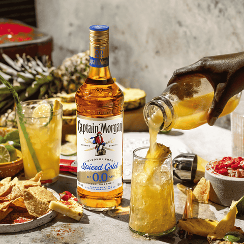 Captain Morgan Spiced Gold alcohol-free rum being poured into a glass with a tropical setting.