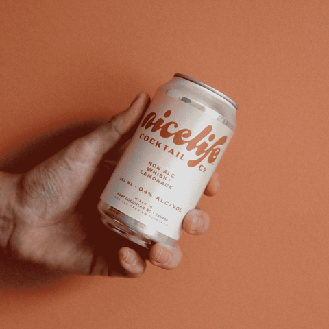 A peron holding a yellow and white can of NiceLife Cocktail Co. non-alcoholic Whisky Lemonade