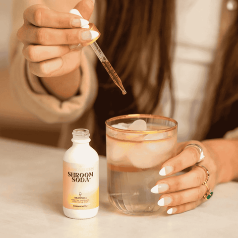 A bottle of Shroom Soda Cream Soda adaptogen mushroom drops being poured into a drink