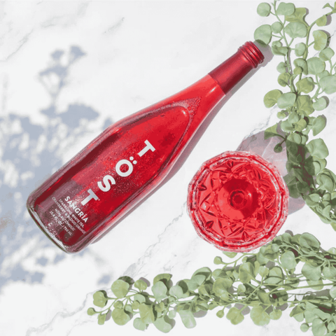 Red bottle of Tost sparkling wine with green leaves on a light background