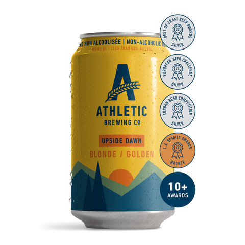 A can of Athletic Brewing Upside Dawn Golden Ale with a yellow label featuring a sun and mountains design. The can indicates it is a non-alcoholic beverage and lists several award badges.