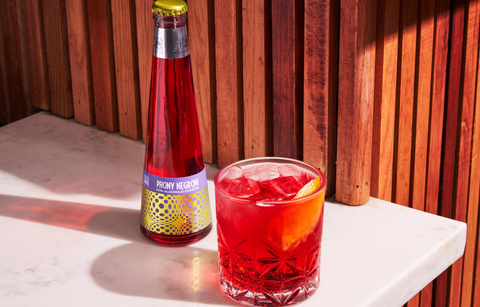 Bottle of ruby red Phony Negroni poured into a cocktail glass with an orange rind on a wooden background