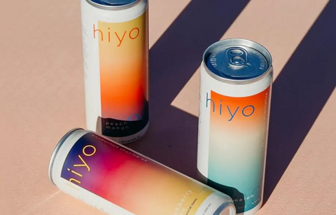 Three 'hiyo' functional drink cans with colorful designs on a two-tone background