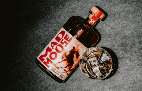 a designed bottle of Mad Moose non-alcoholic whiskey with a glass of whiskey on a dark surface