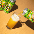 A hand pouring Jelly King non-alcoholic beer from a green and orange patterned can into a glass on a wooden table.