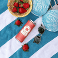 A pink can of Casa Pinata Strawberry Shrub on a blue and white towel with a bowl of strawberries