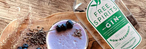 Bottle of Free Spirits Gin on a wooden surface with a cocktail and garnishes.
