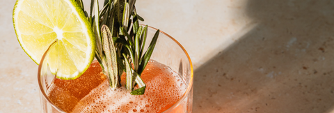 Cocktail with lime and rosemary garnish on a textured surface