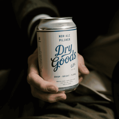 A person holding a can of Dry Goods Non-Alcoholic Pilsner