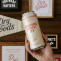 A person holding a can of Dry Goods non-alcoholic Tangerine Apricot IPA