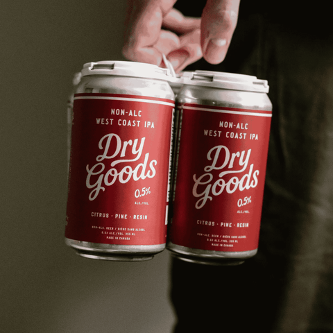 A person holding a 4-pack of Dry Goods West Coast IPA Non-Alcoholic Beer