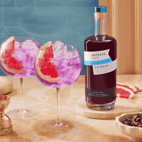 Bottle of Empress 1908 0.0 Indigo with two grapefruit cocktails on a table.