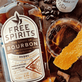 A bottle of Free Spirits non-alcoholic Bourbon on a wooden table with coffee beans and a non-alcoholic cocktail