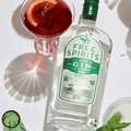 A bottle of Free Spirits non-alcoholic Gin on a white table, with a non-alcoholic blood orange and gin cocktail