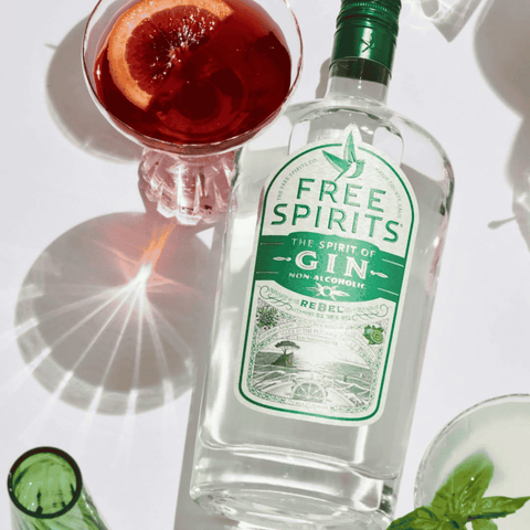 A bottle of Free Spirits non-alcoholic Gin on a white table, with a non-alcoholic blood orange and gin cocktail