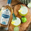 A bottle of Free Spirits non-alcoholic Tequila on a wood table with limes, pineapples, and a non-alcoholic cocktail