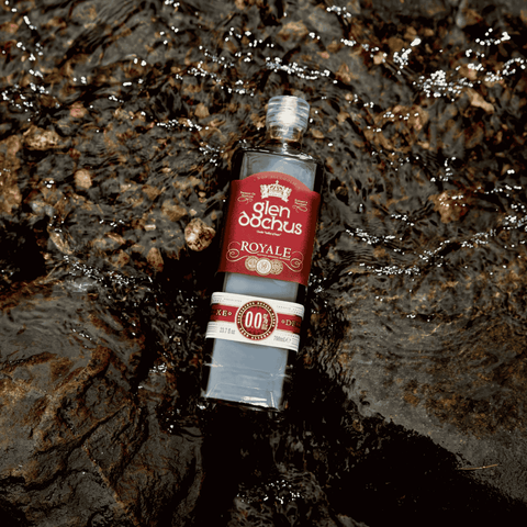 A bottle of Glen Dochus Royale Blend Non-Alcoholic Whiskey displayed in  a riverbed