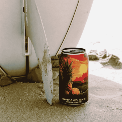 A single can of non-alcoholic pineapple yuzu radler by Go Brewing, beside a surfboard