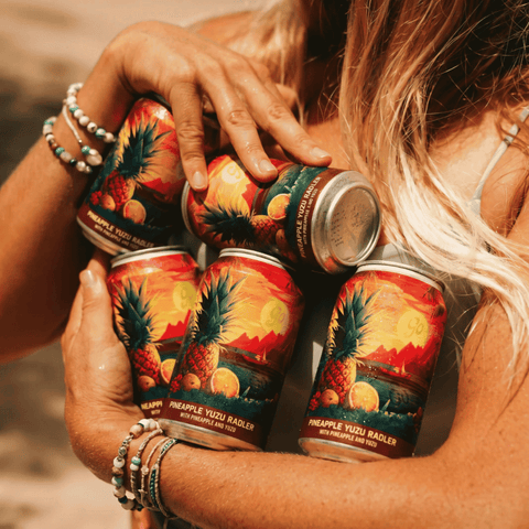 A person holding several cans of non-alcoholic pineapple yuzu radler bu Go Brewing.