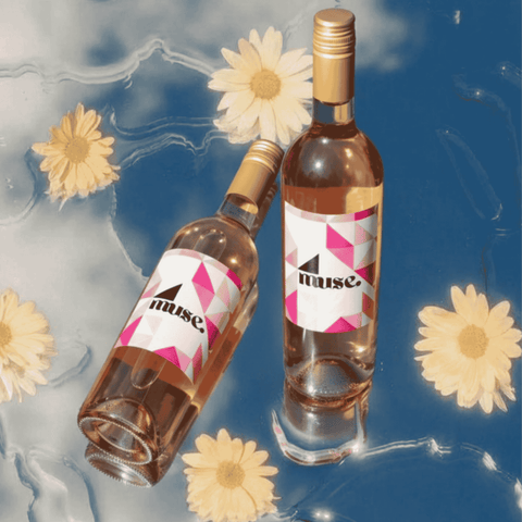 Two bottles of 'muse' wine with floral decorations on a blue and gray background