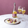 A bottle of Saicho Sparkling Darjeeling Tea with two glasses and a grilled meat dish