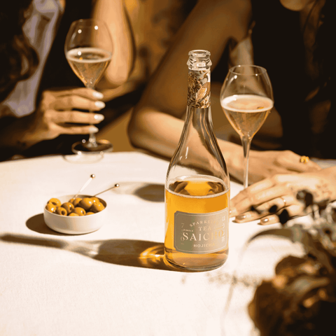 A bottle of Saicho Sparkling Hojicha Tea on a table with green olives