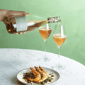 A bottle of Saicho Sparkling Hojicha Tea being poured into two glasses paired with a prawn dish