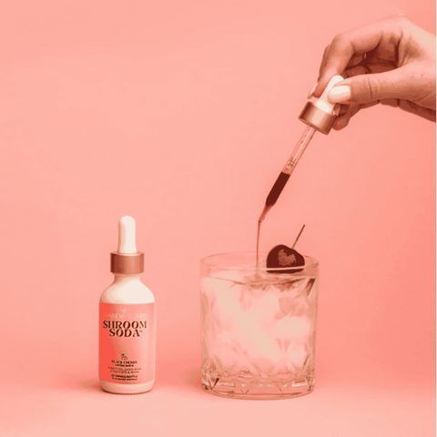 A bottle of Shroom Soda Black Cherry being poured into sparkling water