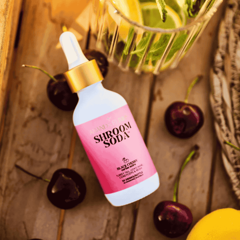 A bottle of Shroom Soda Black Cherry on a table with cherries and lime