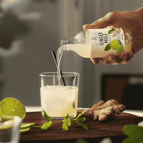A bottle of Sir James 101 non-alcoholic Ginger Mule bing poured into a rocks glass with ginger and lime