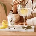 A bottle of Sir James 101 non-aloholic Gin and Tonic poured into a glass with lemon, juniper, and rosemary