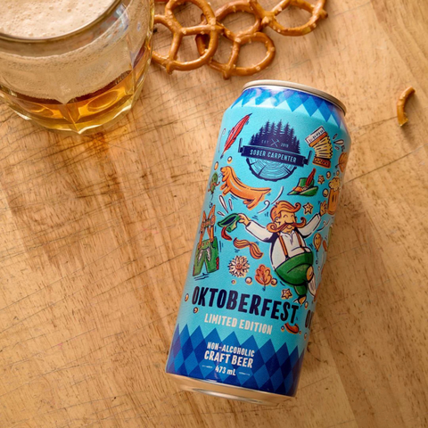 A blue can of Sober Carpenter non-alcoholic Oktoberfest beer, staged with pretzels and a mug of beer
