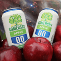 Two cans of Somersby Zero Apple non-alcoholic cider surrounded by red apples.
