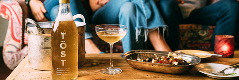 Person sitting at a table with a bottle of Töst non-alcoholic sparkling tea, and food.