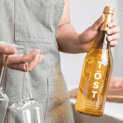 Person holding a bottle of TOST sparkling white tea with two glasses.