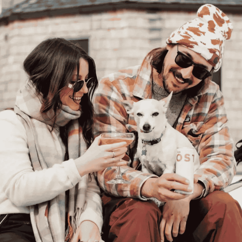 Two people sitting, one holding a dog, the other a can of TOST Original Sparkling Tea