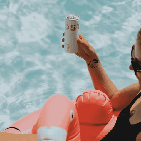 A person in  a pool holding a can of TOST Original Sparkling Tea