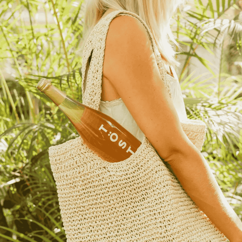 A Woman holding a woven bag with a bottle of TOST Original Sparkling White Tea