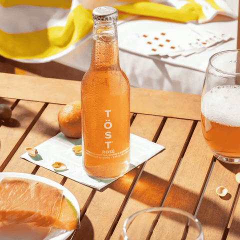 A bottle of TOST Rose Sparkling White Tea displayed on a summer patio