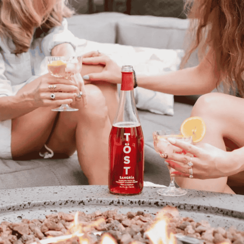 Two people sitting outdoors with a bottle of TOST Sangria between them.