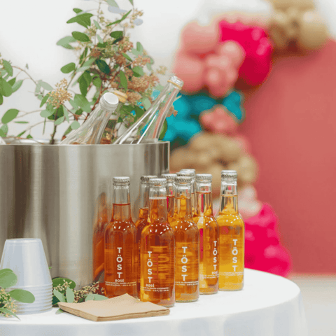 Bottles of TÖST rose non-alcoholic sparkling tea on a table with decorative flowers for a wedding